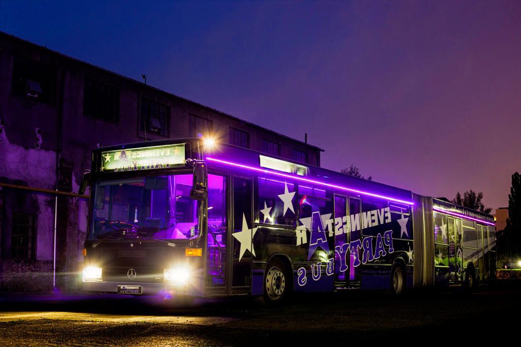 70 seater party bus Budapest with purple neon lighting parked at night, ideal for large group events.