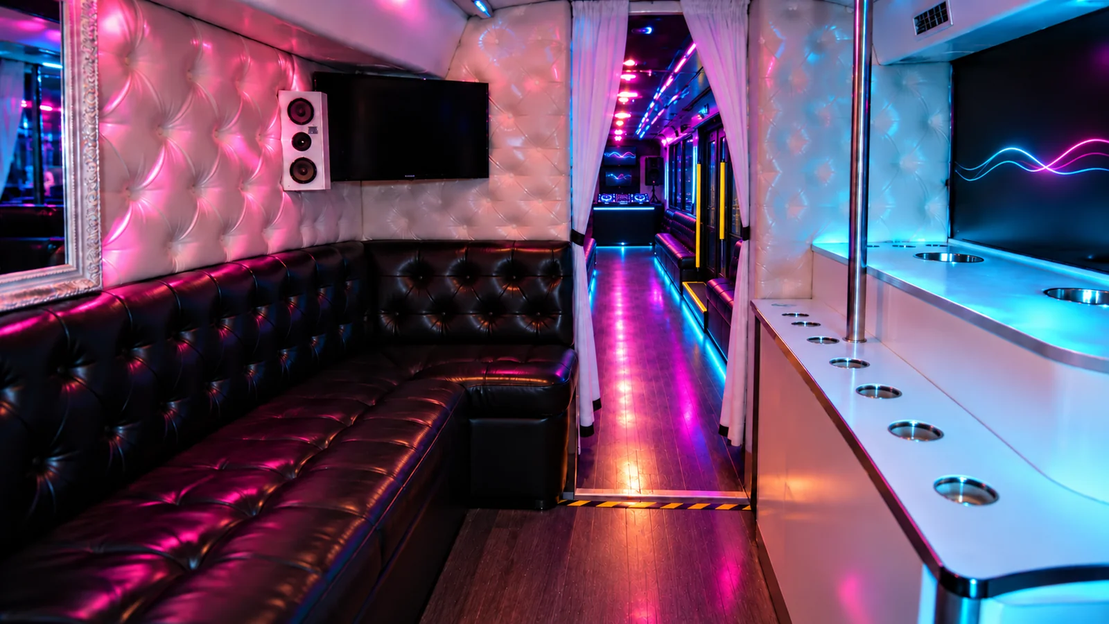 Private party bus lounge with black leather sofas, a white bar and side benches beyond the curtains